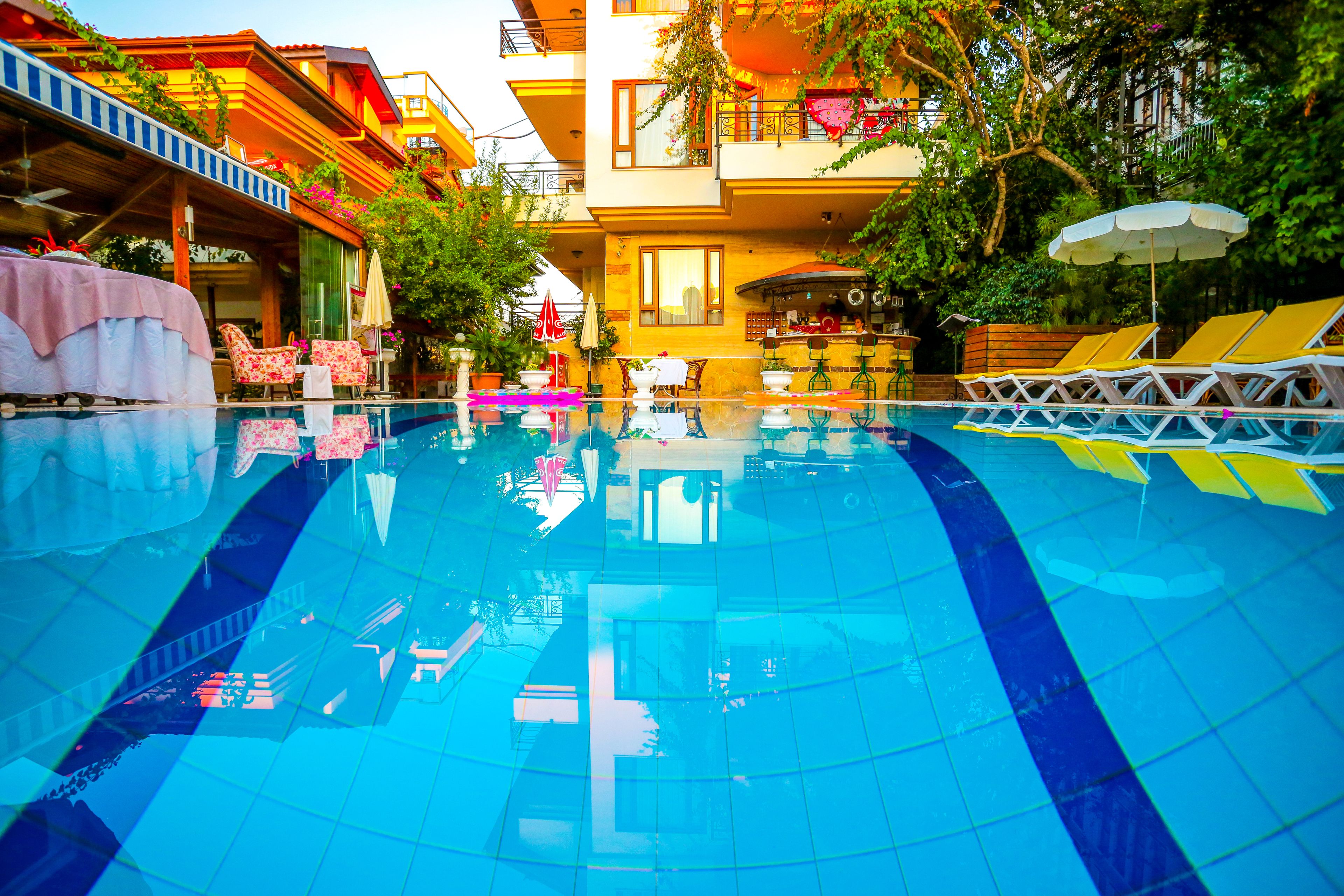 A swimming pool with lounge chairs and a table, surrounded by a building with balconies and plants.