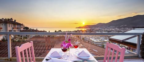 A table set for two with a sunset view, two chairs, and a vase of flowers.