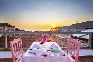 Mesa lista para dos con vista al atardecer, dos sillas y un jarrón de flores.