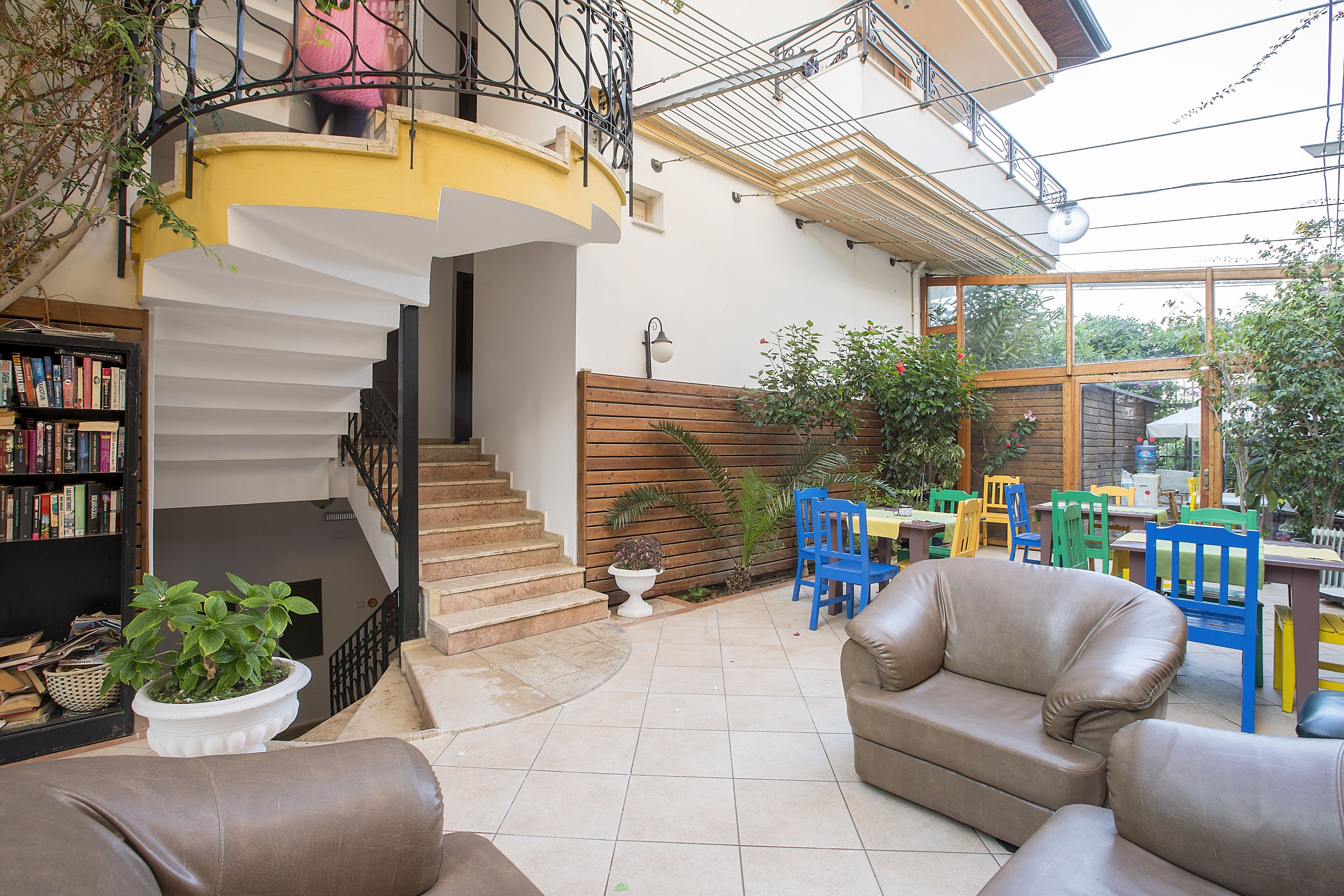 A spacious living area with a staircase, a dining area with colorful chairs, and a bookshelf.