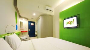 Een hotelkamer met een bed, een groene accentmuur, een televisie waarop het logo van 'pop! HOTELS' staat, en een badkamer met een blauwe deur.