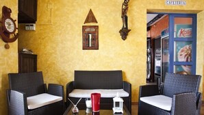 A cozy seating area with wicker chairs and a small table, a wall clock, and a sign for 'CAFETERIA'. - Hotel Atalaya (Nijar)