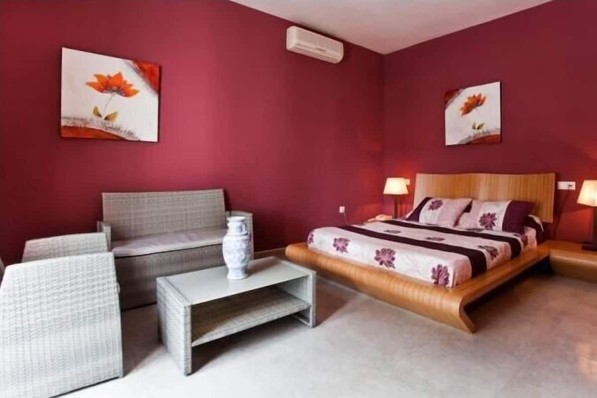 A bedroom with a bed, bedside tables, a sofa, and two wall-mounted paintings.