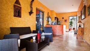 A hotel lobby with wicker furniture, a reception desk, and a door leading to the rooms. - Hotel Atalaya (Nijar)