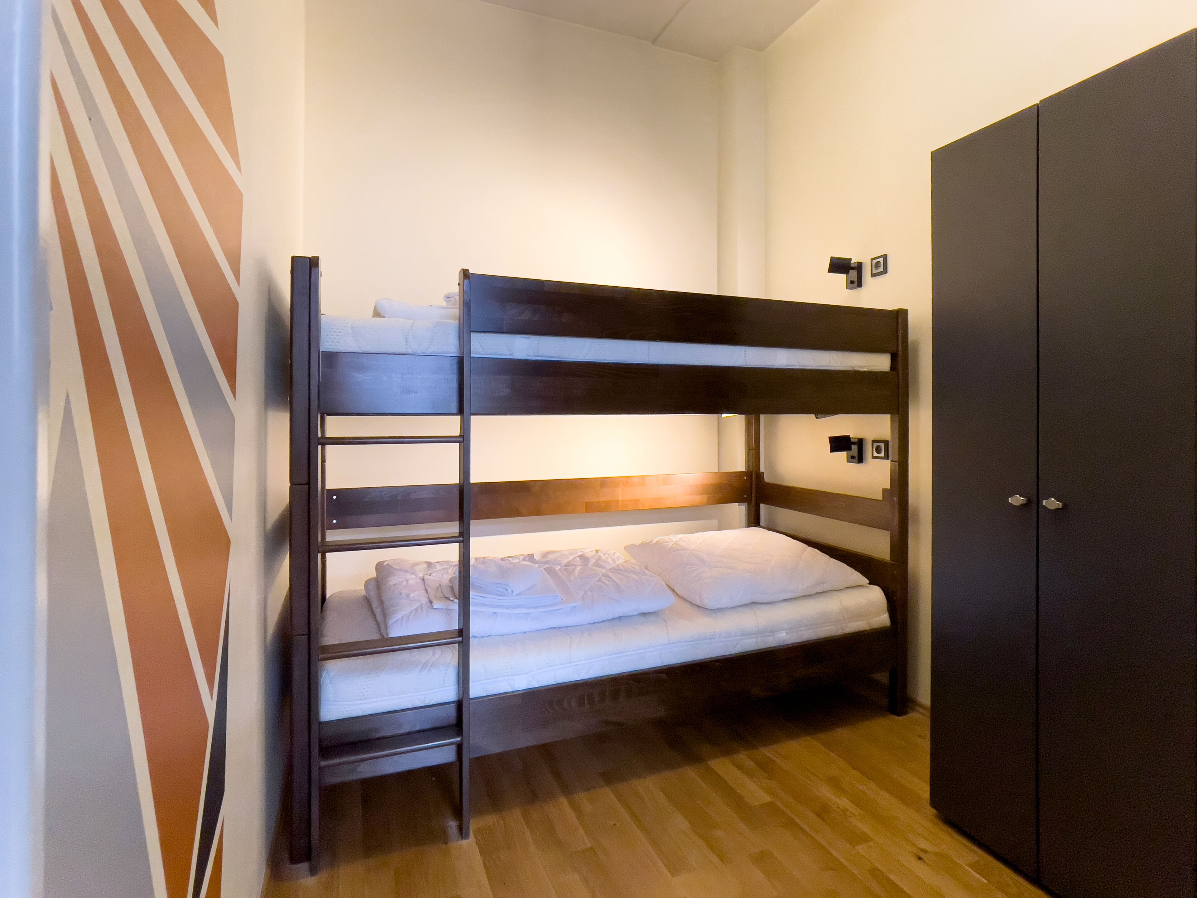 Ein Stockbett mit Holzbettrahmen, ein Kleiderschrank und eine gestreifte Wand.