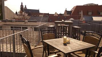 Una terraza en la azotea con mesas de madera y sillas de mimbre, con vistas a edificios históricos.