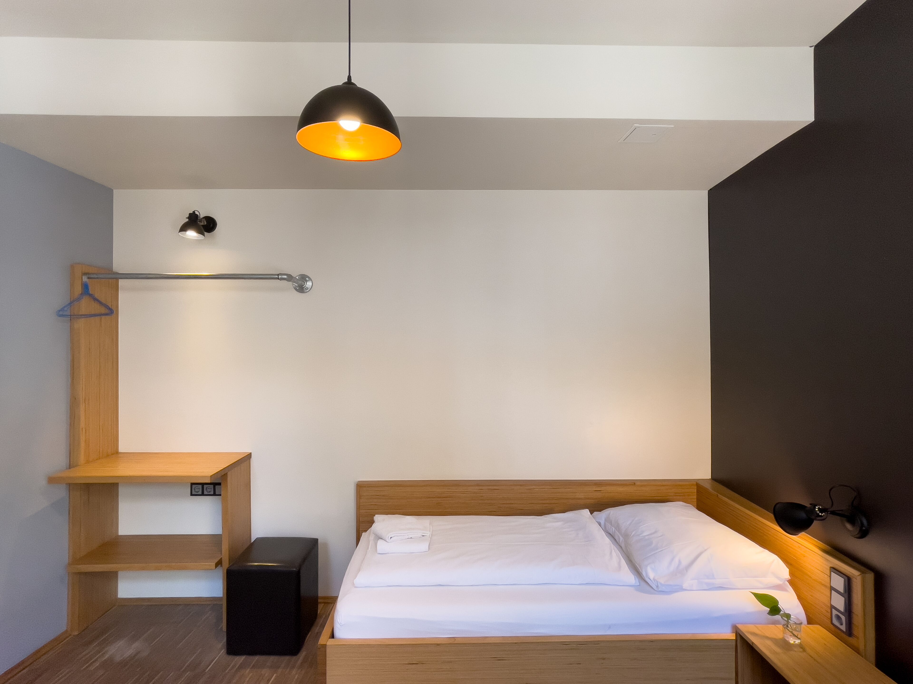 Une chambre à coucher moderne avec un lit en bois, une table de chevet, un luminaire suspendu et une étagère fixée au mur.