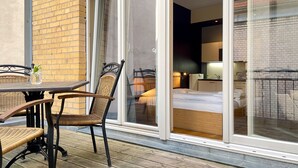 A hotel room with a large sliding glass door, a wicker table, and chairs, and a bed with white linens.