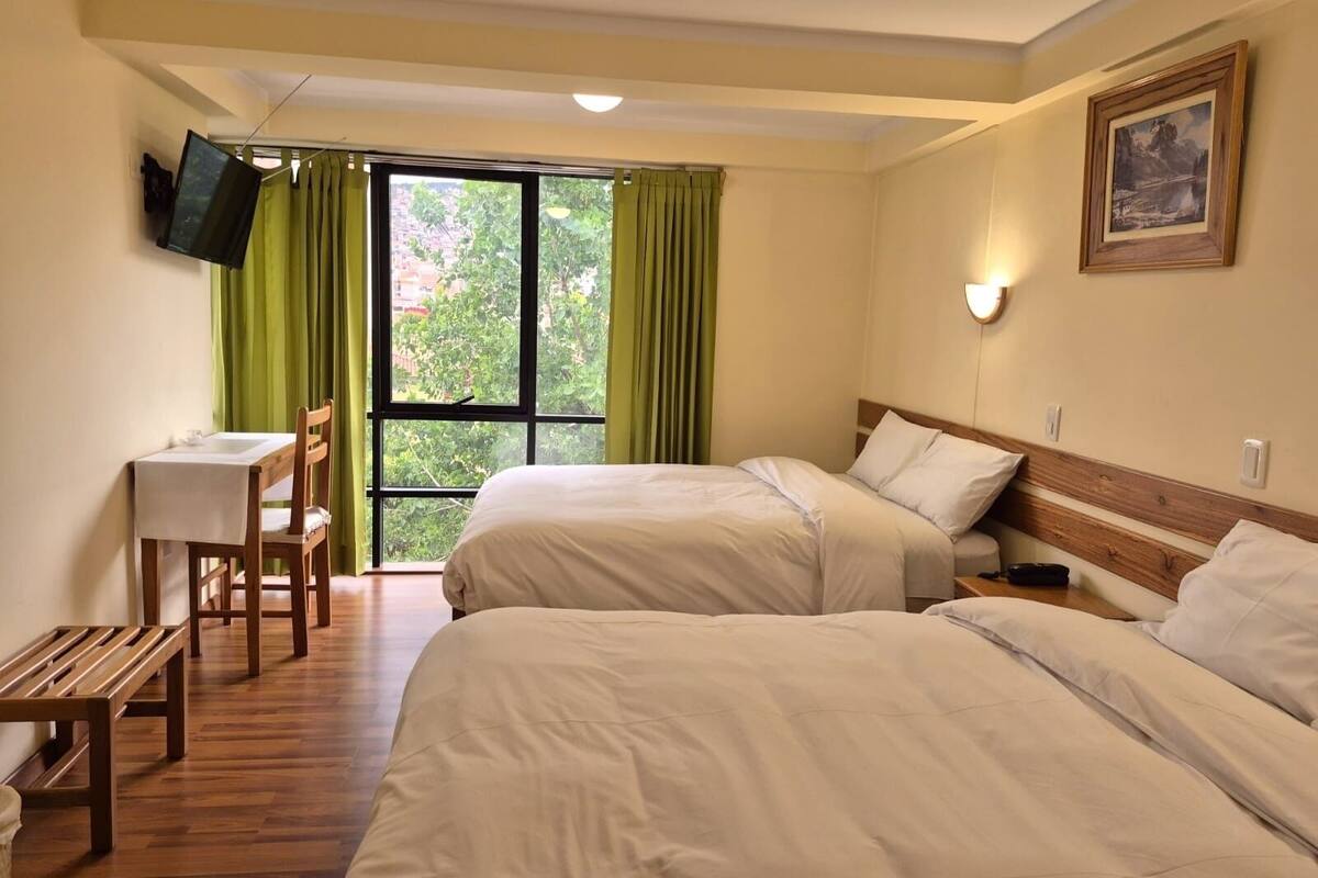 A hotel room with two beds, a desk, a chair, and a television mounted on the wall.