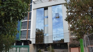 A modern building with a glass facade reflecting the sky, a gated entrance, and a staircase leading to the entrance. - Florida del Inca Hotel (Cusco)