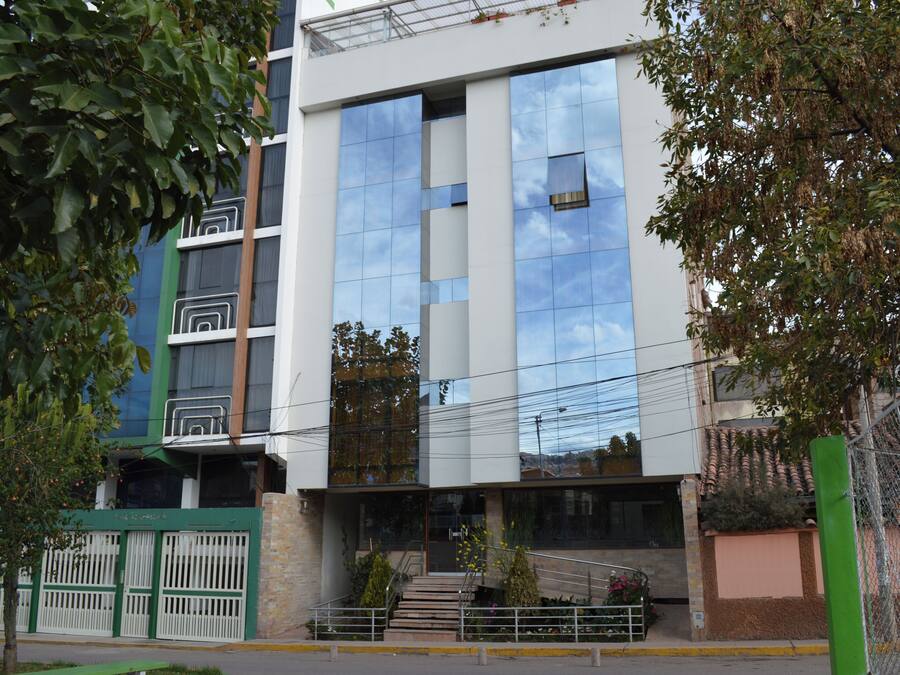 Un edificio moderno con fachada de vidrio que refleja el cielo, una entrada con portón y una escalera que conduce a la entrada.