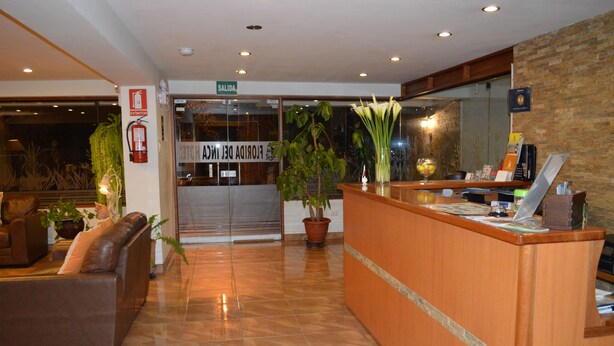 A hotel reception area with a wooden reception desk, a leather sofa, and potted plants. - Florida del Inca Hotel (Cusco)