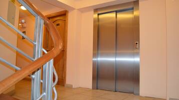 Een moderne lift met een metalen afwerking, een houten deur en een metalen handrail in een gang.