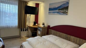 Una habitación de hotel con cama, escritorio con computadora, silla, ventana con cortinas, un cuadro de un lago y un cabecero rojo.