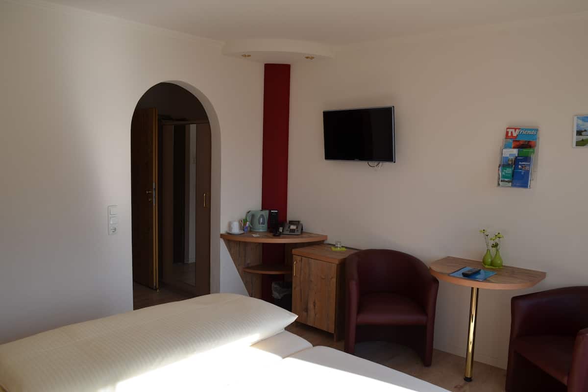 A hotel room with a bed, a desk with a computer, a TV, and two chairs.