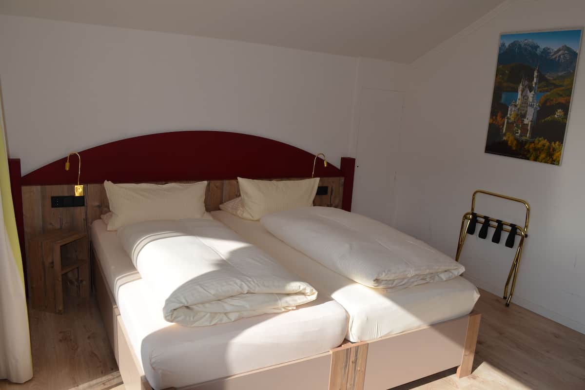 A double bed with white linens, a wooden headboard, and a wall-mounted rack.