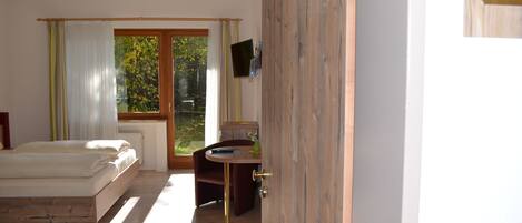 Un dormitorio con cama de madera, una mesita de noche, una ventana con cortinas, un escritorio con silla y un baño con lavamanos y espejo.