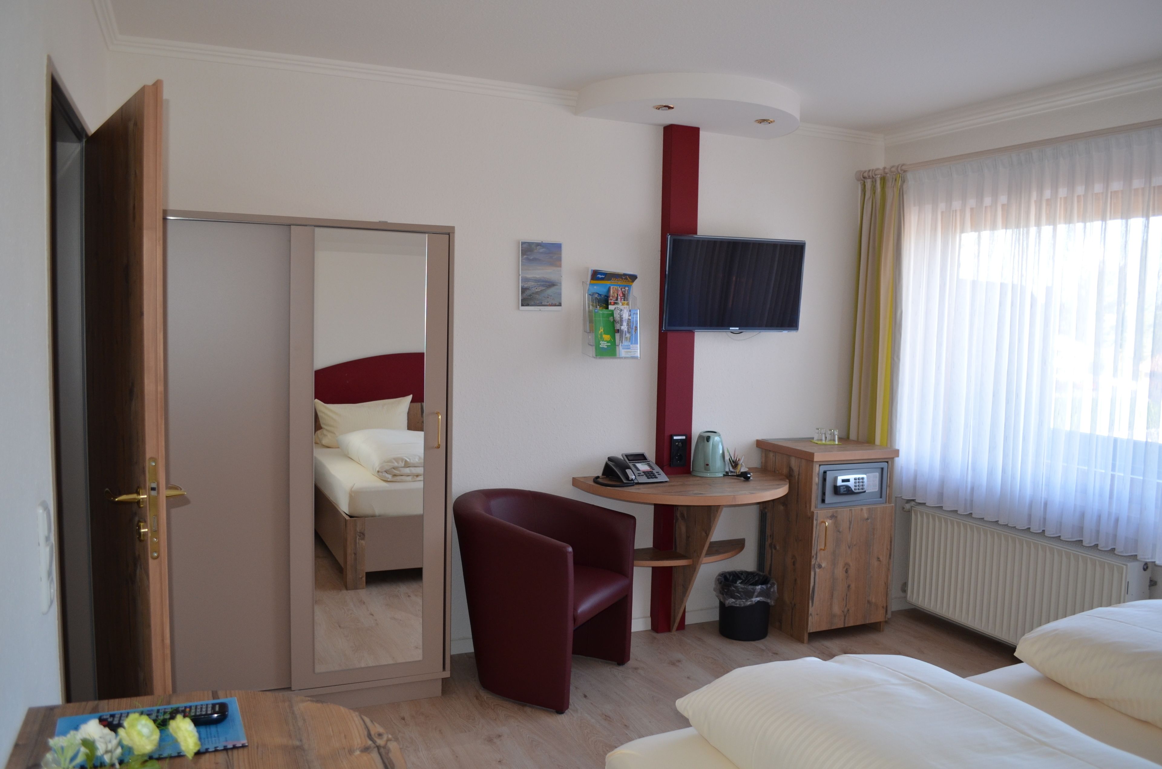 Una habitación de hotel con cama, escritorio con teléfono, silla, televisor montado en la pared y ventana con cortinas.