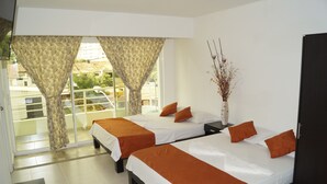 A hotel room with two beds, a nightstand, a vase with dried flowers, and a view of the outside.