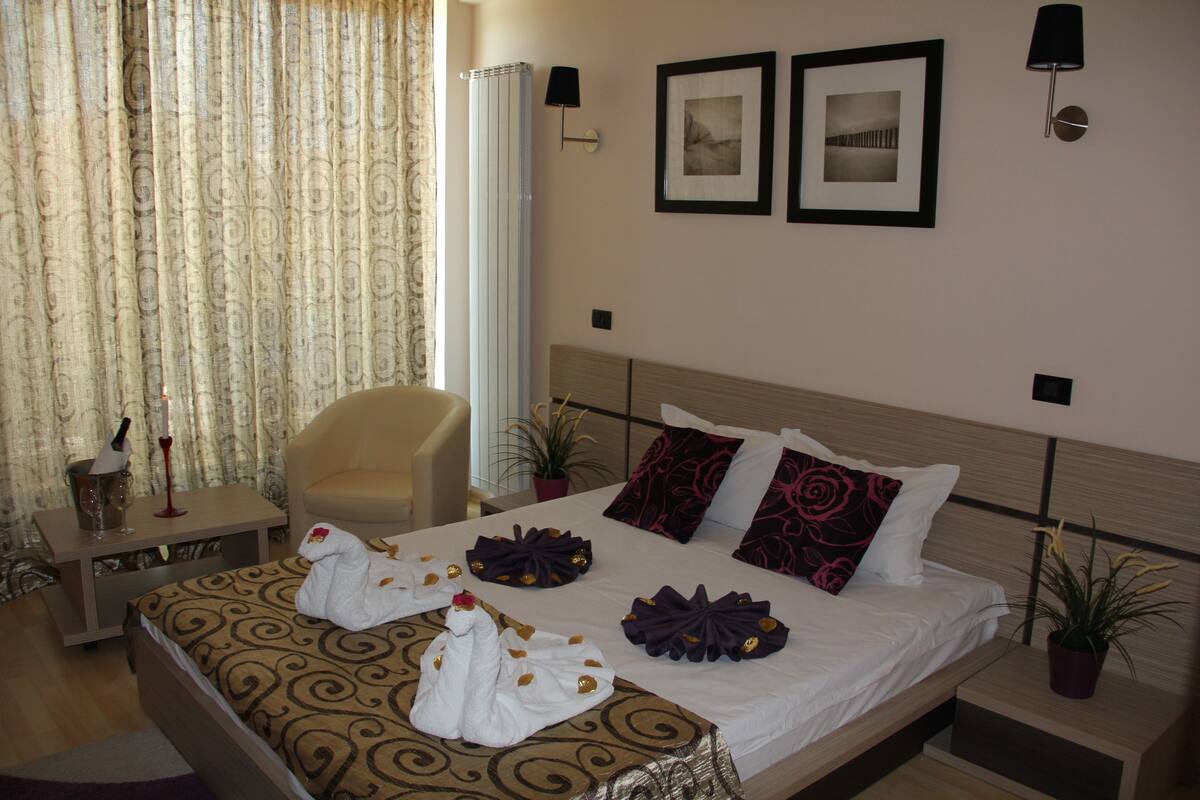 A neatly made bed with patterned bedding, a bedside table with a lamp, and two framed pictures on the wall.