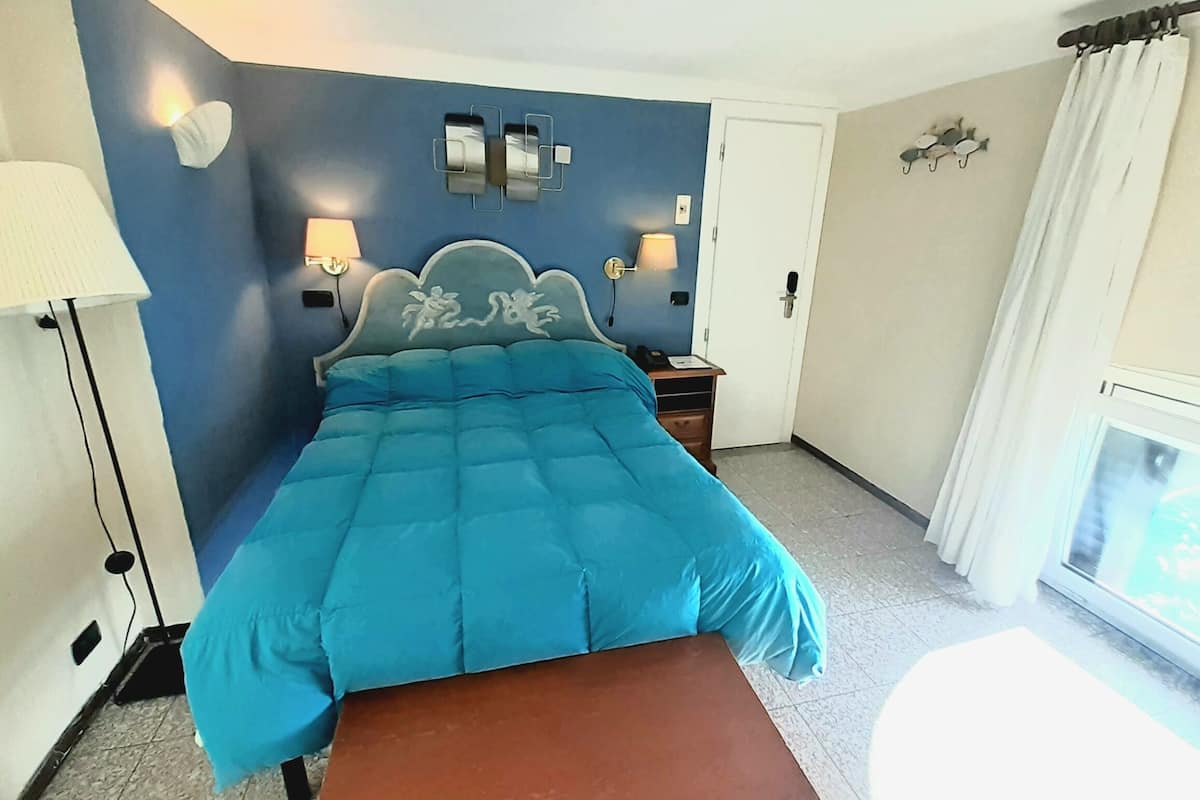 A bedroom with a bed, bedside lamps, a nightstand, a bench, and a window with curtains.