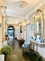 Un hall d’hôtel avec un comptoir d’accueil, un grand miroir, une chaise et une plante en pot.