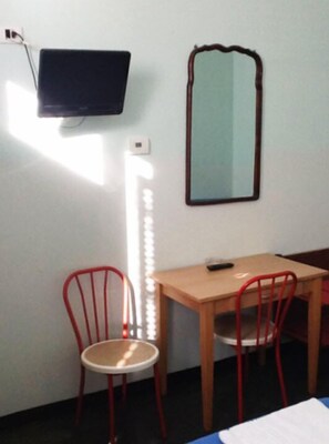 Een kamer met een bed, een bureau, twee rode stoelen, een televisie, een spiegel en een bedlamp.