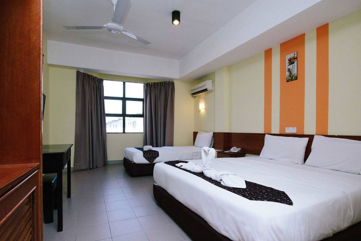 Een hotelkamer met een groot bed, twee kleinere bedden, een bureau en een plafondventilator.