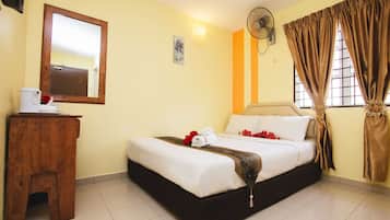 Una habitación de hotel con cama, un taburete de madera, un espejo, un ventilador y cortinas.