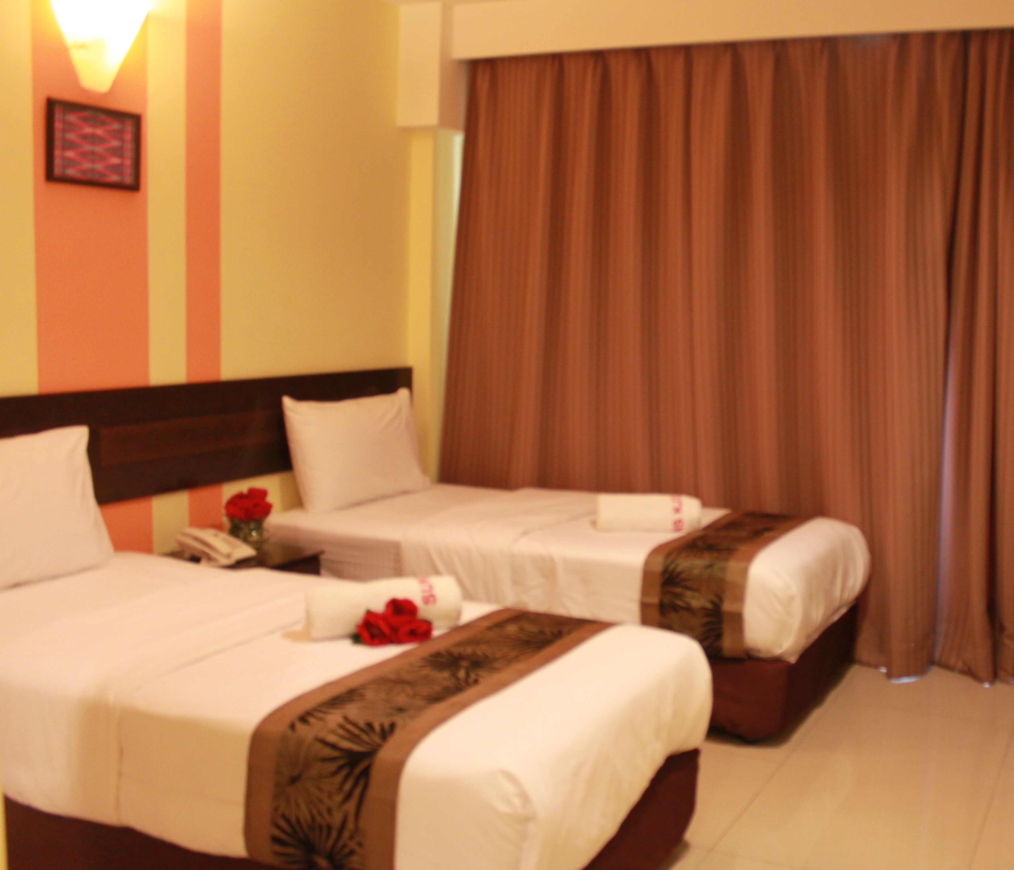 A hotel room with two beds, a nightstand, and a curtain.