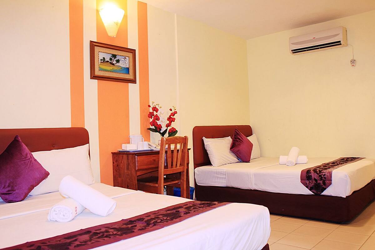 Een hotelkamer met twee bedden, een bureau, een stoel, een foto aan de muur en een airconditioning.