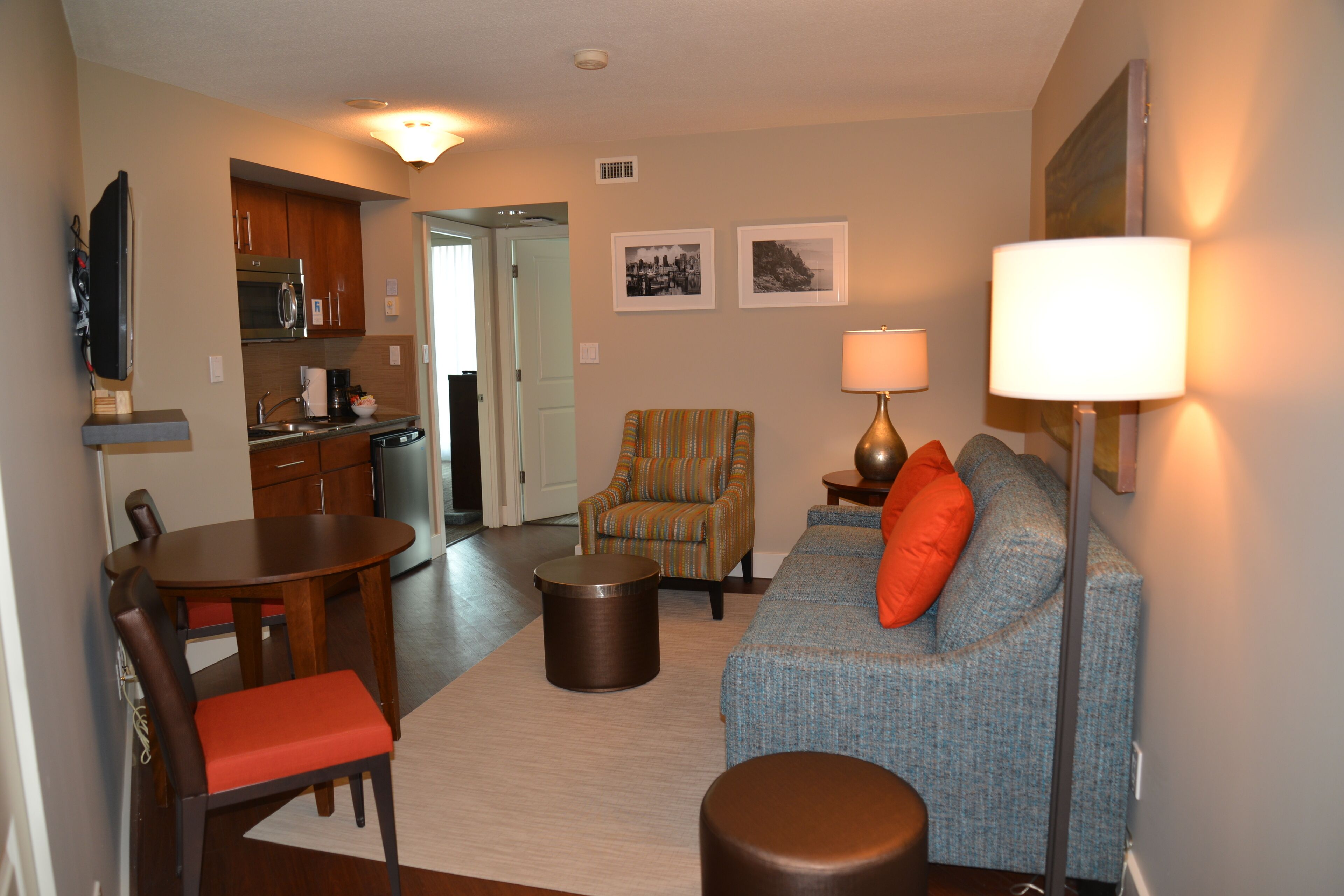 A living room with a sofa, armchair, coffee table, and dining table. There is a kitchen in the background.
