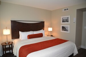 Quarto de hotel com uma cama grande, duas luminárias laterais e uma cabeceira.