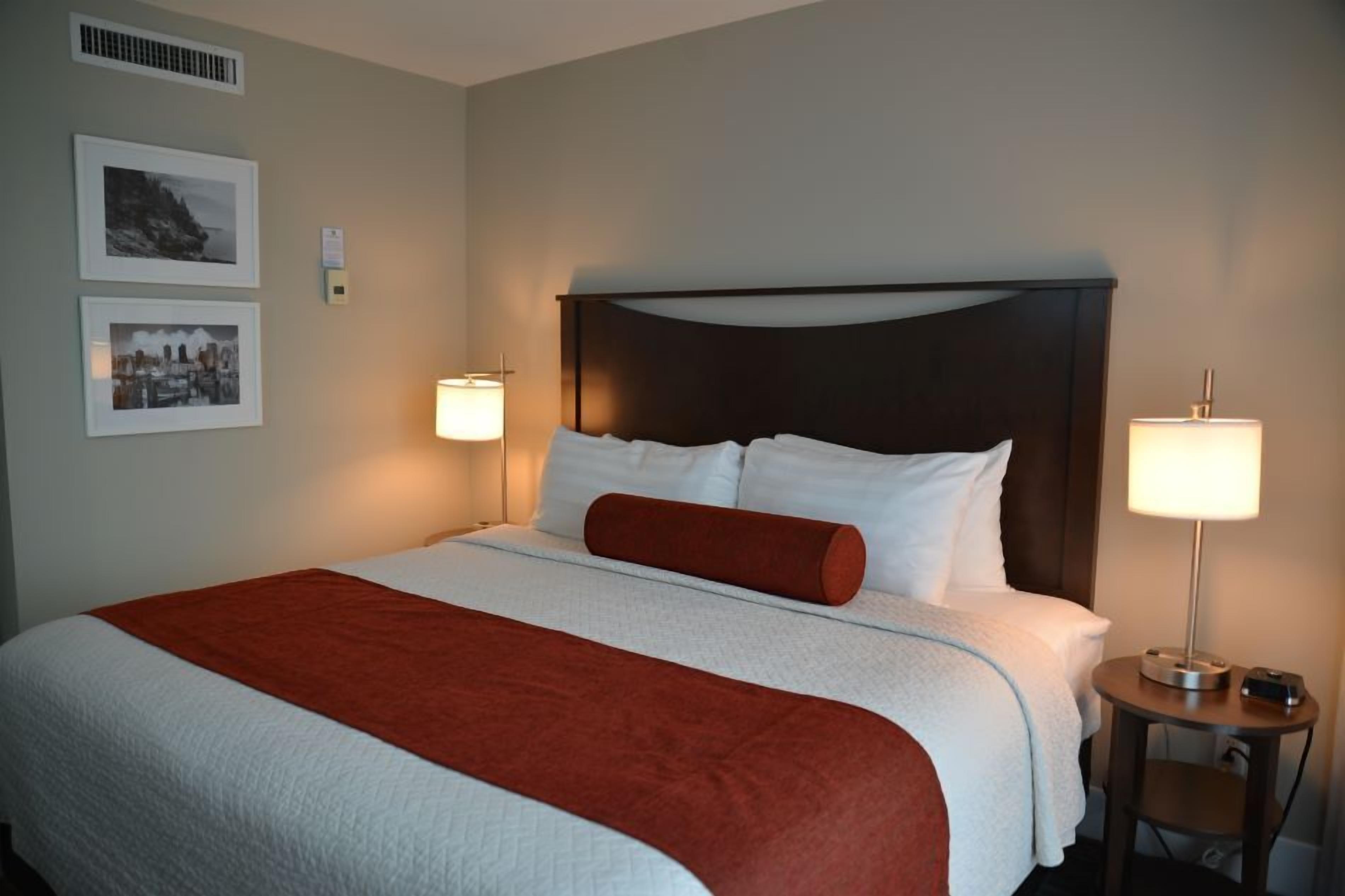 A neatly made bed with white and red bedding, two bedside lamps, and framed pictures on the wall.