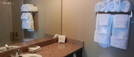 A bathroom with a sink, mirror, towel rack, toilet, and a shower area.