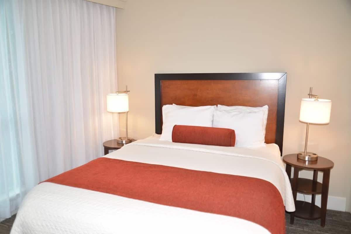 A hotel room with a large bed, two bedside lamps, a wooden headboard, and a white curtain.