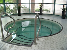 An indoor swimming pool with clear water, tiled floor, and metal handrails.