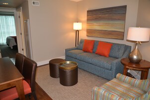 A hotel room with a blue sofa, orange cushions, a wooden table, two cylindrical side tables, and a lamp.