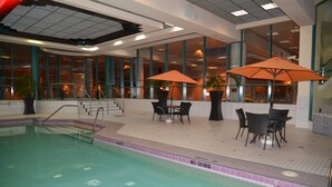 An indoor swimming pool with a tiled edge, surrounded by a seating area with tables and chairs, and large windows providing views of the interior. - Rosedale Condominiums (Vancouver)