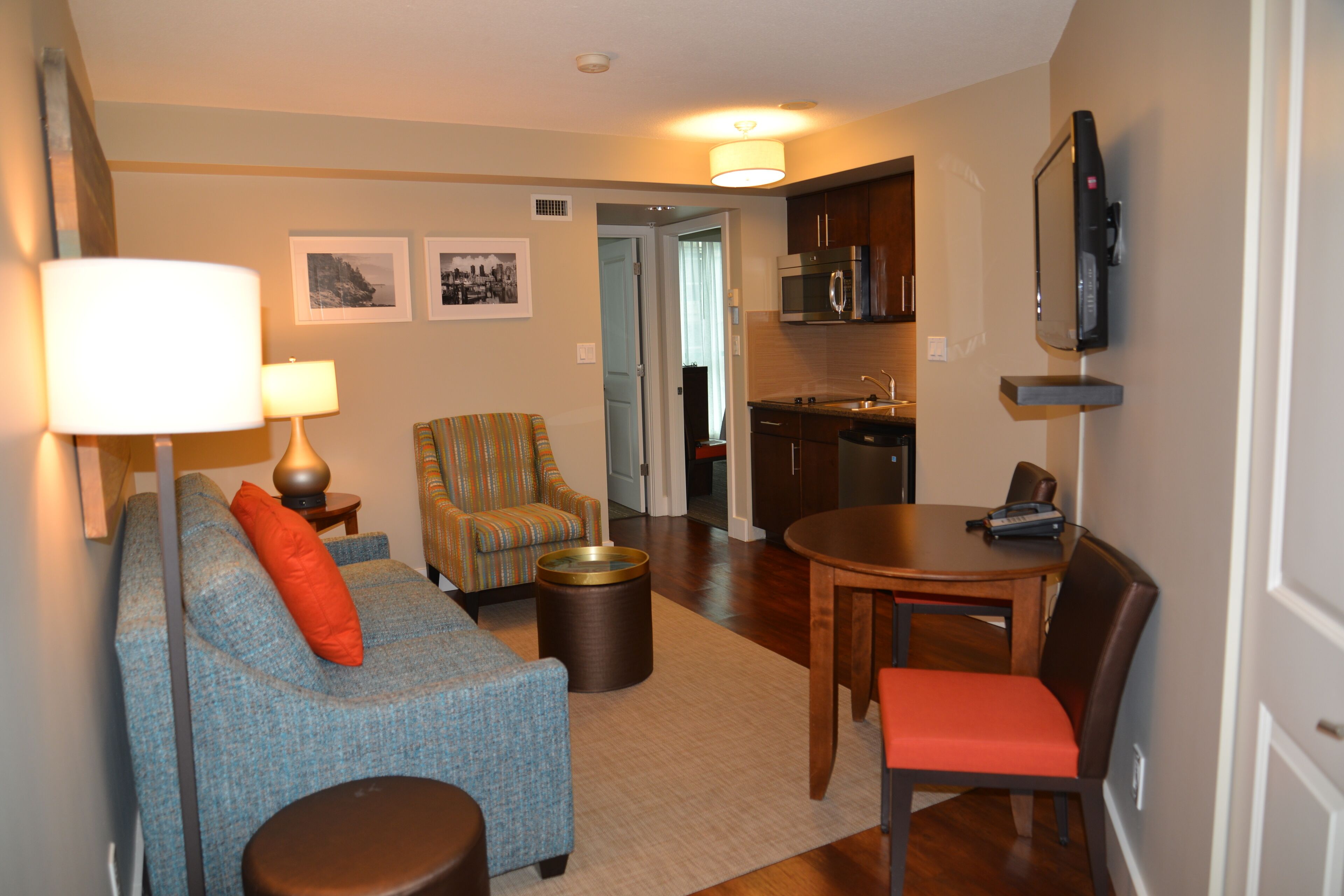 A living room with a sofa, armchair, and a dining table with chairs. There is a kitchen area with cabinets and a microwave.