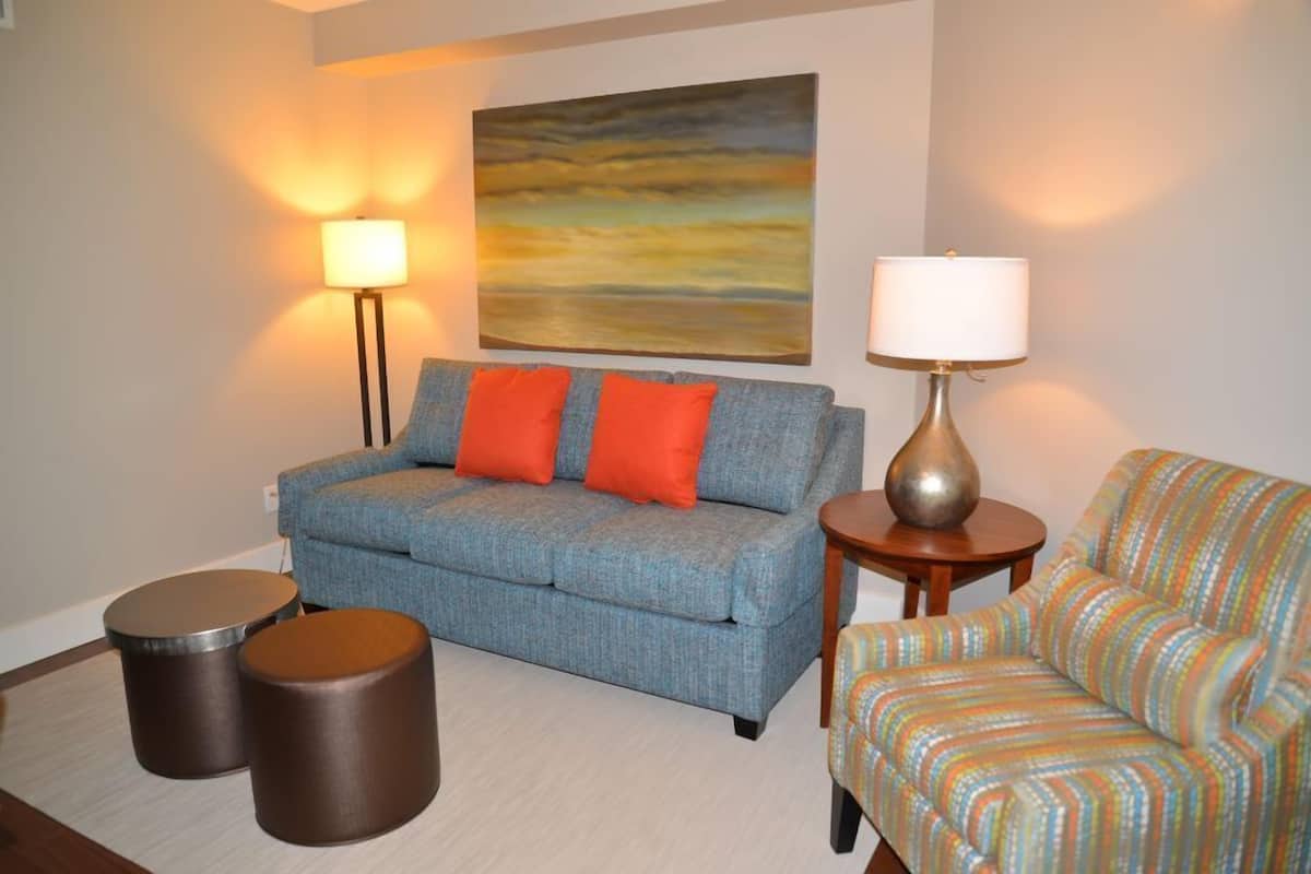 A living room with a sofa, two round stools, a lamp, and a colorful chair.