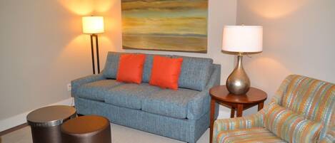 A living room with a sofa, two round stools, a lamp, and a colorful chair.