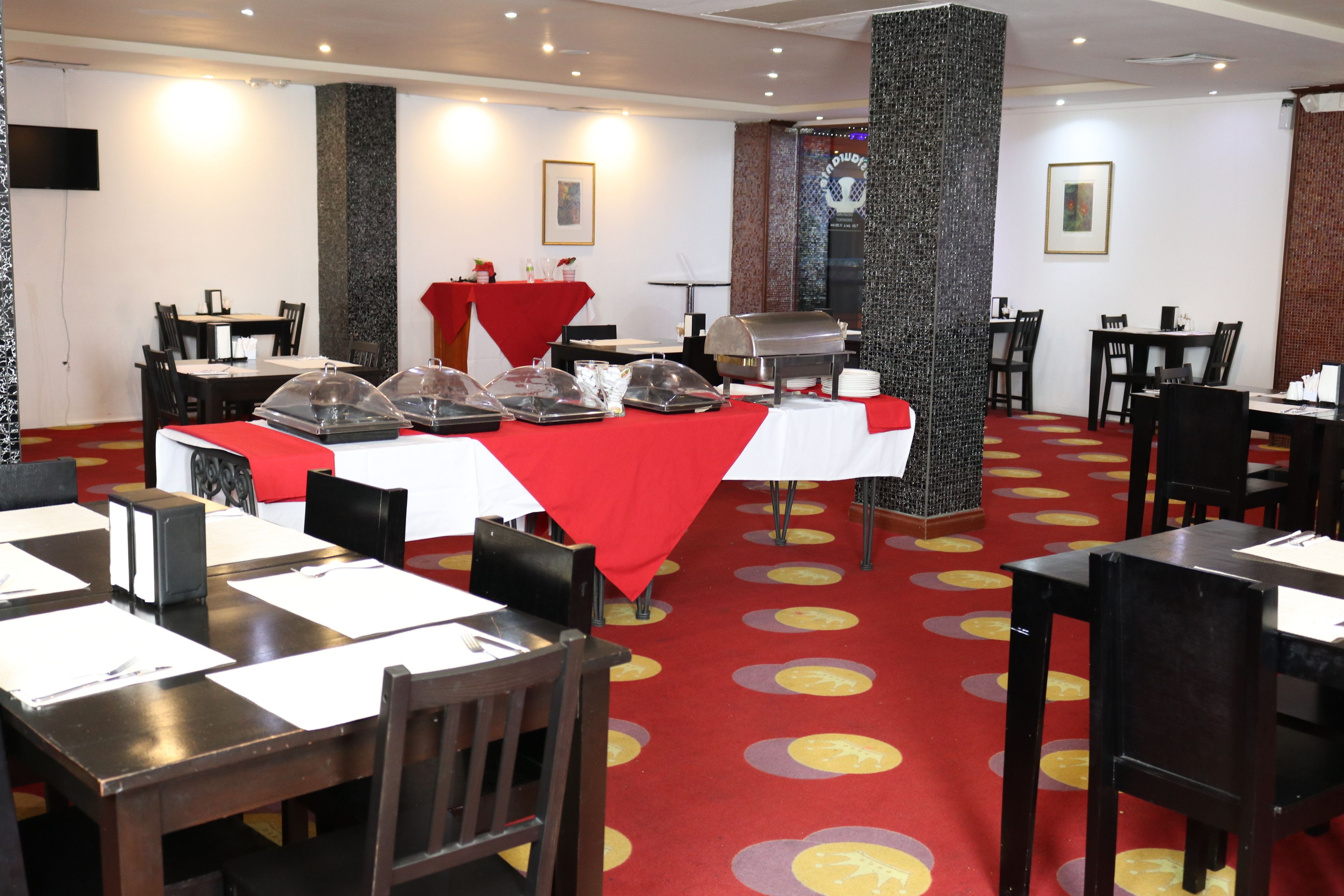 Un comedor con mesas cubiertas con manteles rojos, sillas y un puesto para buffet.