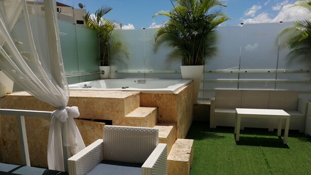 Terraza en la azotea con jacuzzi, mobiliario de mimbre y césped artificial.