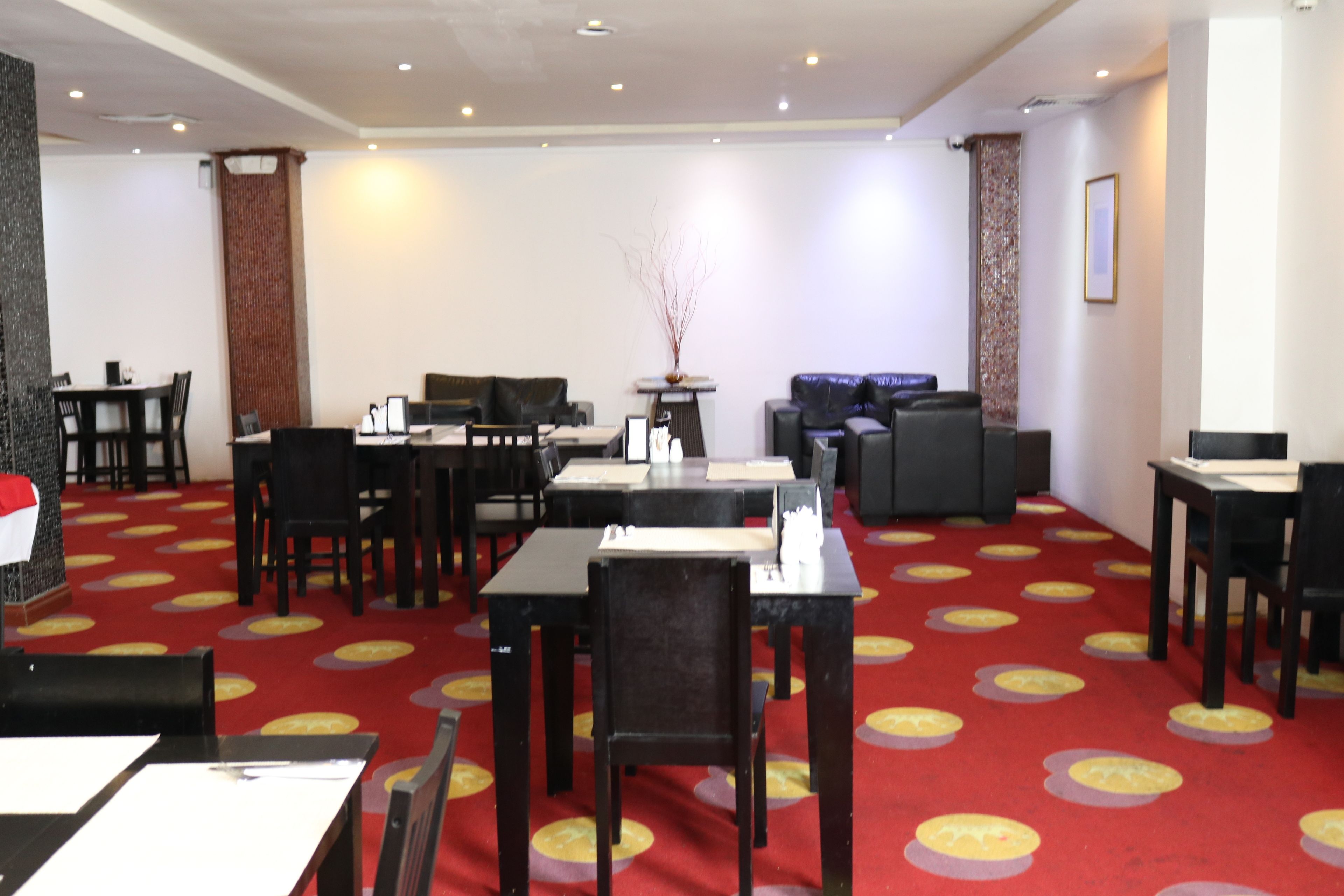 A hotel lobby with multiple seating areas, including a dining area with tables and chairs, a sofa, and a small table with a vase.