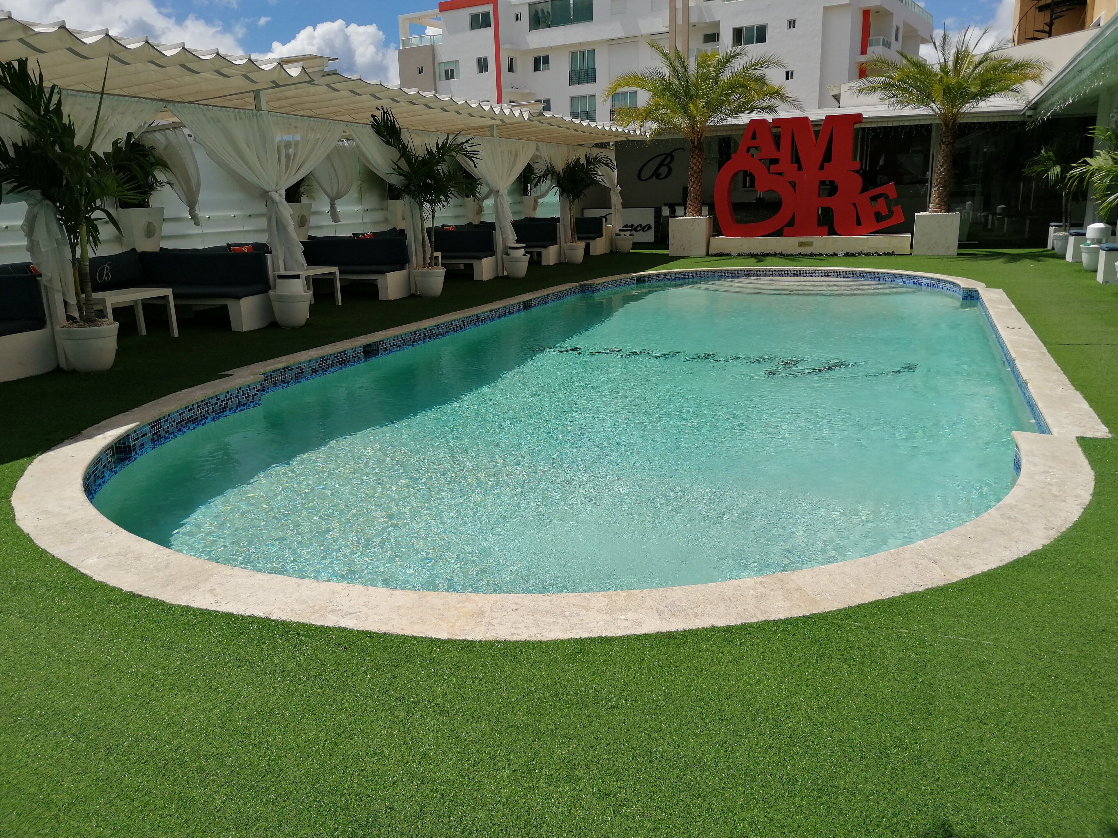 A swimming pool with a tiled edge, surrounded by artificial grass and potted plants.