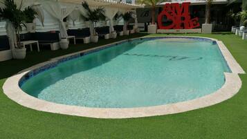 A swimming pool with a tiled edge, surrounded by artificial grass and potted plants.