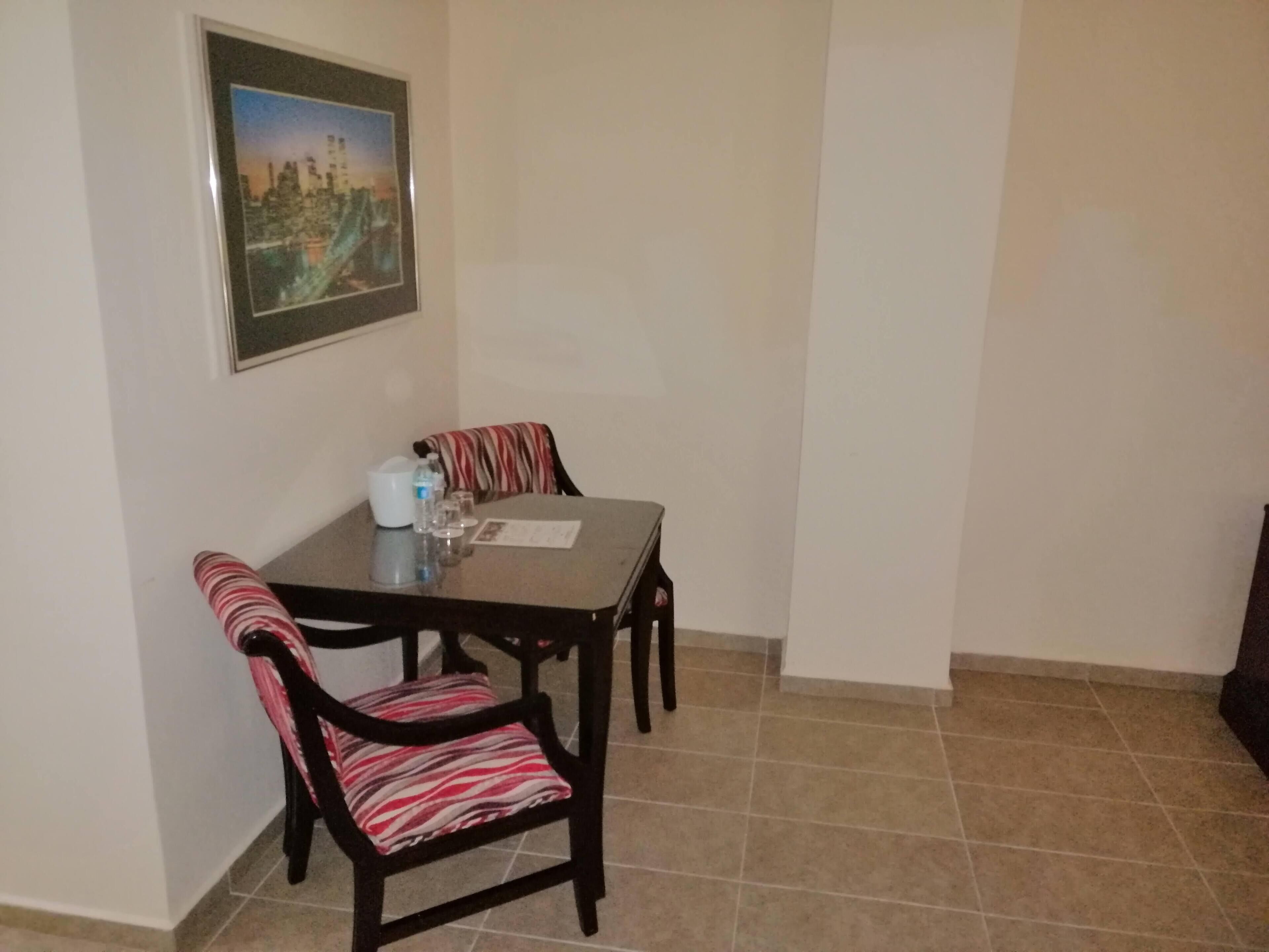 A dining area with a table and two chairs, a framed picture on the wall, and a tiled floor.
