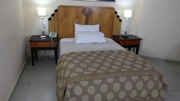A hotel room with a bed, two bedside tables, a nightstand, a lamp, a phone, and a framed picture on the wall.