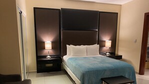 Una habitación de hotel con una cama grande, dos mesitas de noche con lámparas, un banco y una silla.